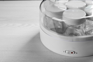 Photo of Modern yogurt maker with empty jars on white wooden table, closeup. Space for text