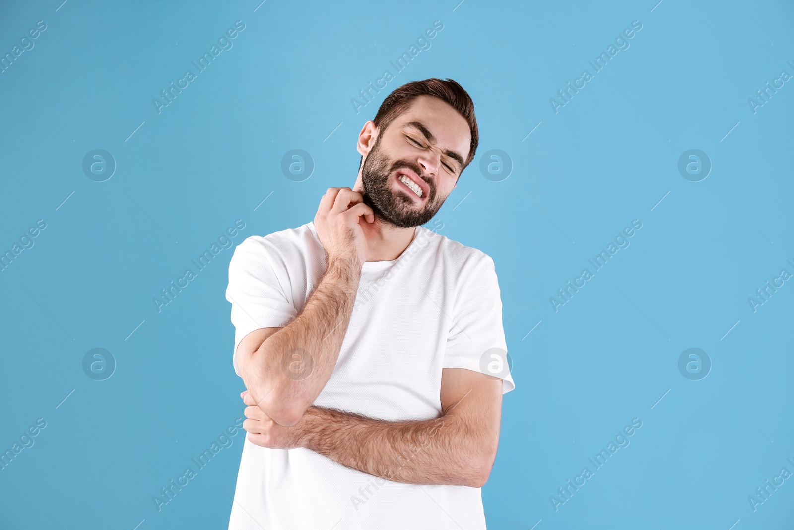 Photo of Young man scratching neck on color background. Allergies symptoms