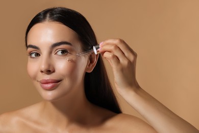 Beautiful young woman applying serum onto her face on beige background. Space for text