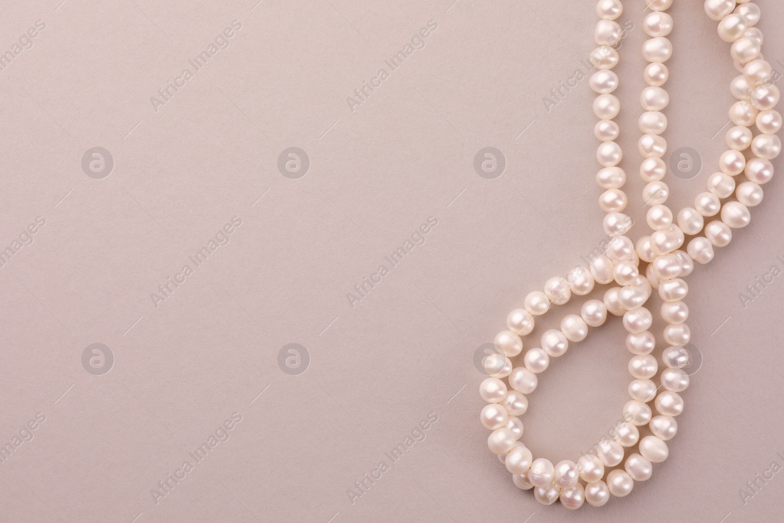 Photo of Elegant pearl necklace on beige background, top view. Space for text