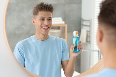 Young man with mouthwash and toothbrush near mirror in bathroom