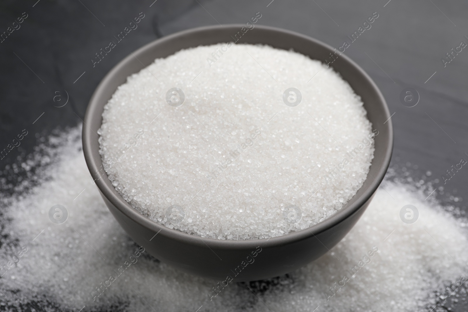 Photo of Granulated sugar on black table, closeup view