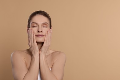 Woman massaging her face on beige background. Space for text
