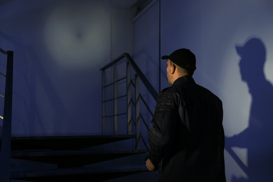 Male security guard with flashlight going up stairs in darkness