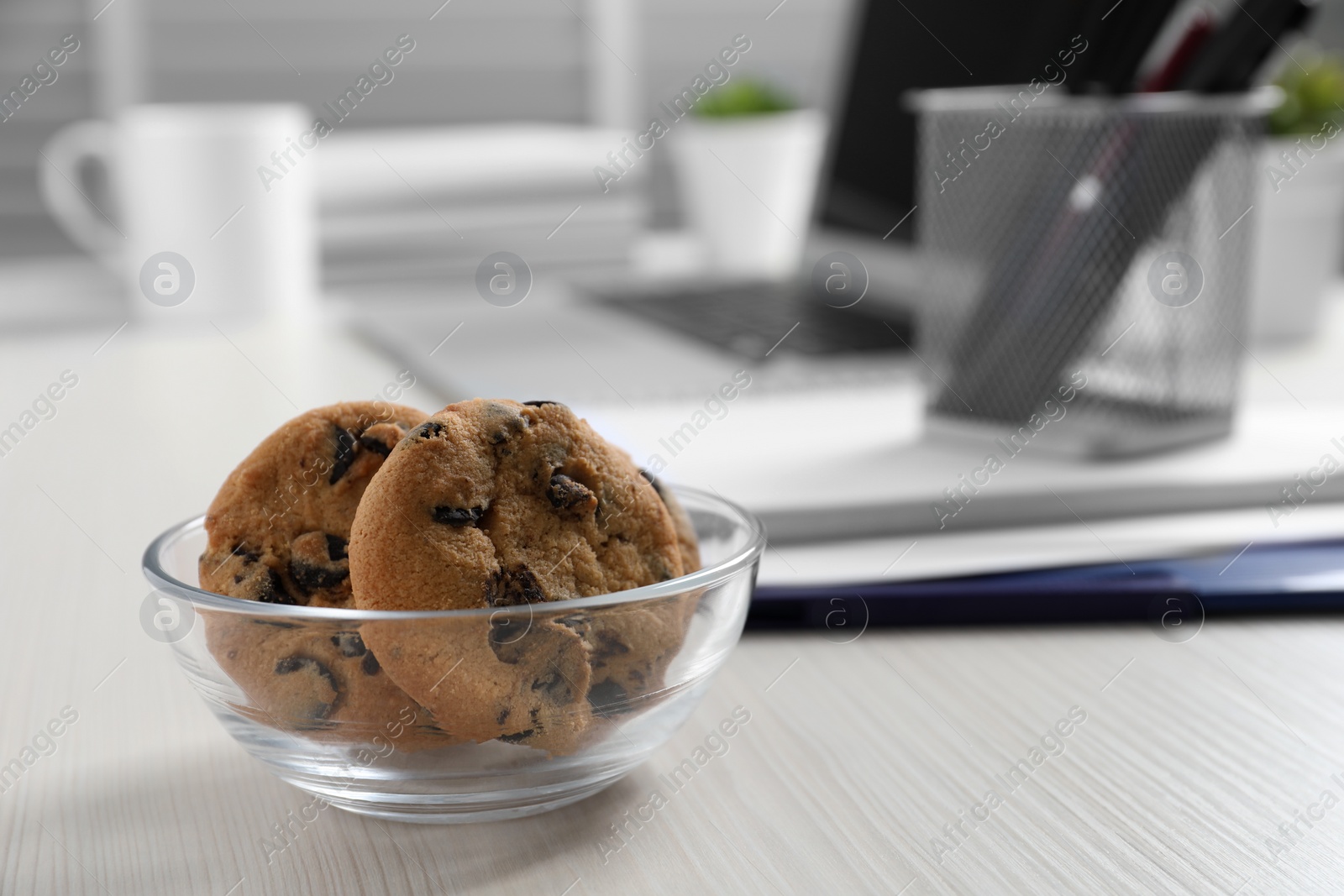 Photo of Bowl with chocolate chip cookies on white wooden table in office. Space for text