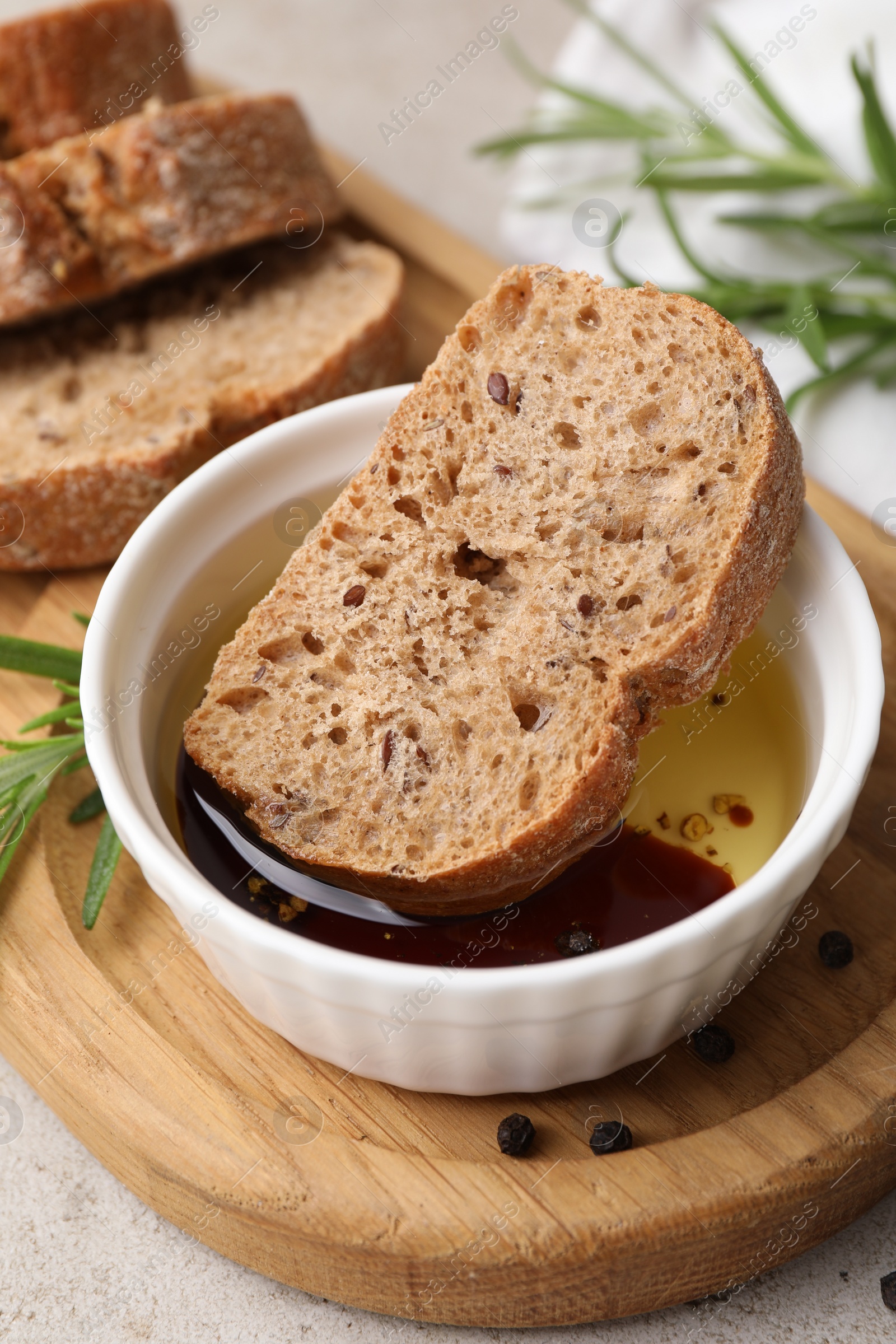 Photo of Bowl of organic balsamic vinegar with oil served with spices and bread slices on beige table, closeup