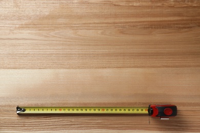 Photo of Tape measure on wooden background, top view. Space for text