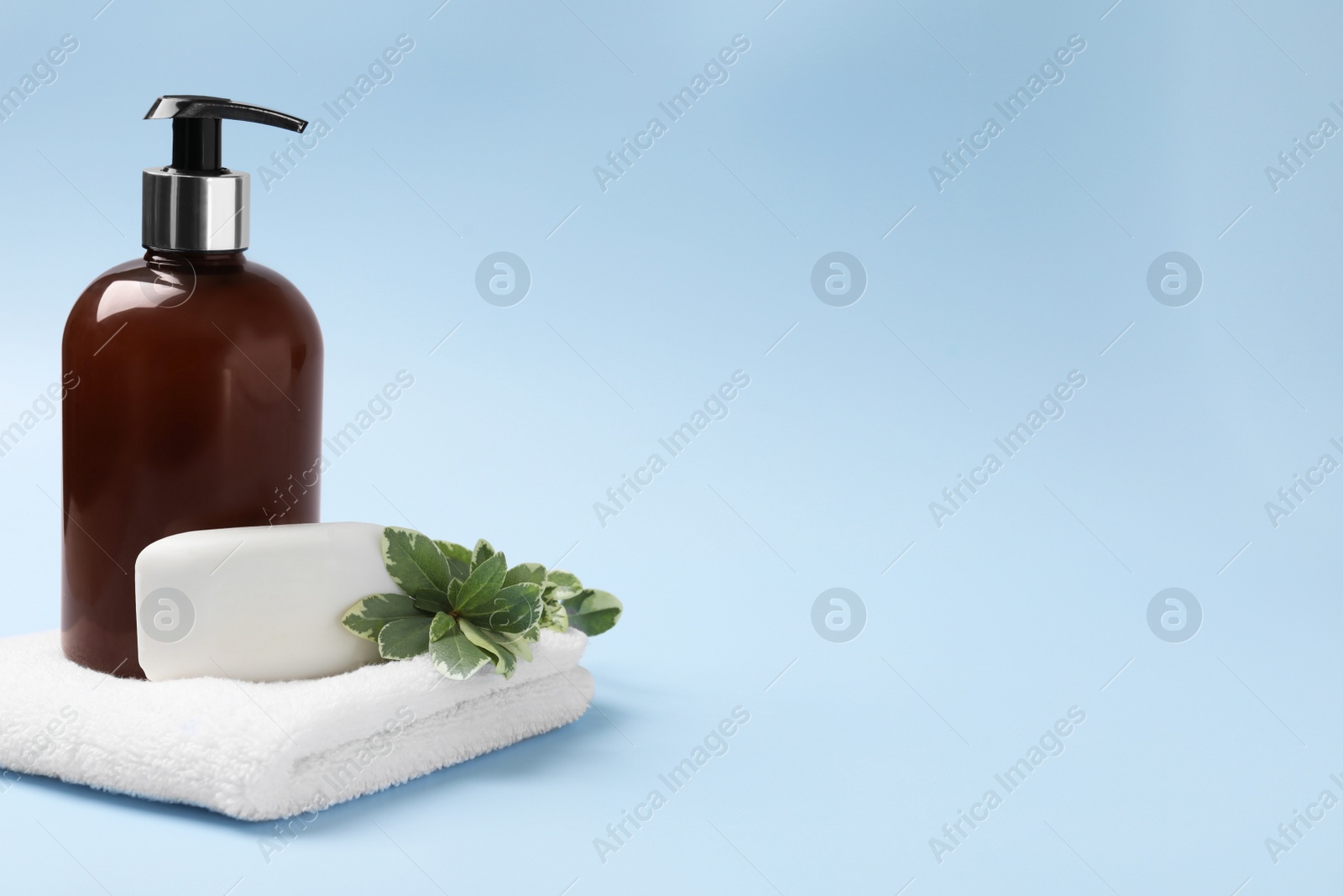 Photo of Soap bar, bottle dispenser and towel on light blue background, space for text