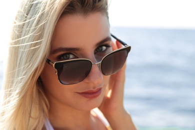 Photo of Beautiful woman wearing sunglasses near sea on sunny day, closeup