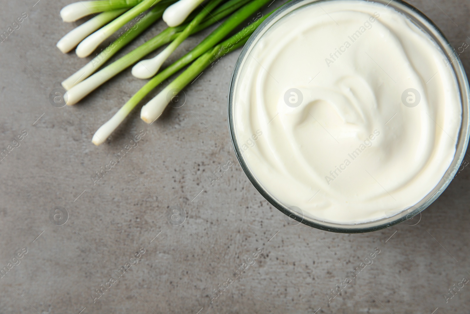 Photo of Glass bowl of fresh sour cream with green onion on grey table, flat lay. Space for text