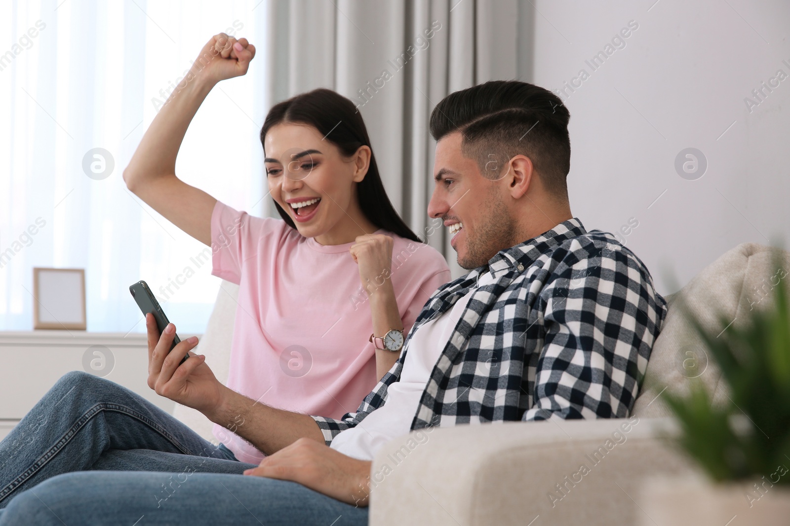 Photo of Emotional couple participating in online auction using smartphone at home