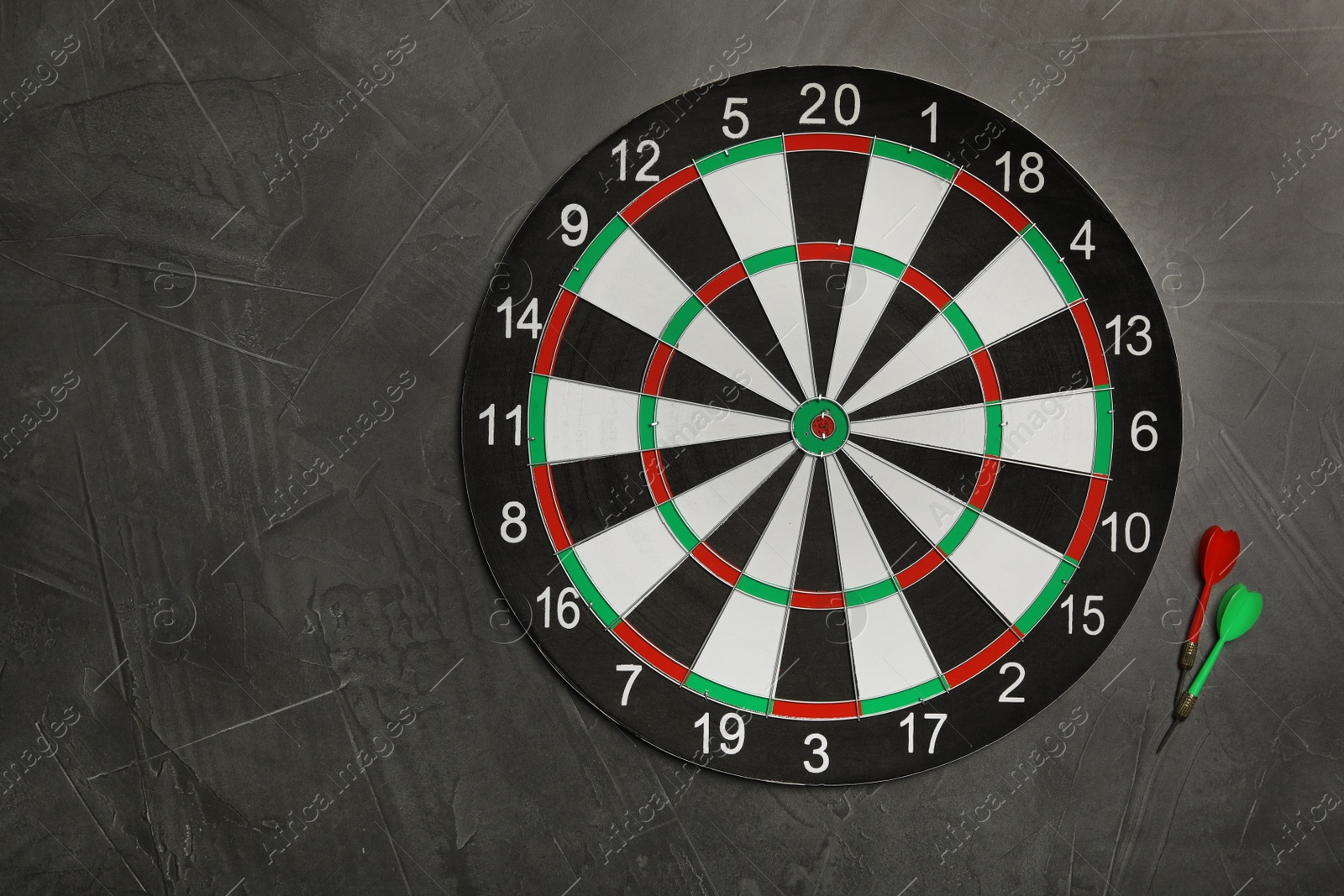 Photo of Dart board with color arrows on grey stone background, top view. Space for text