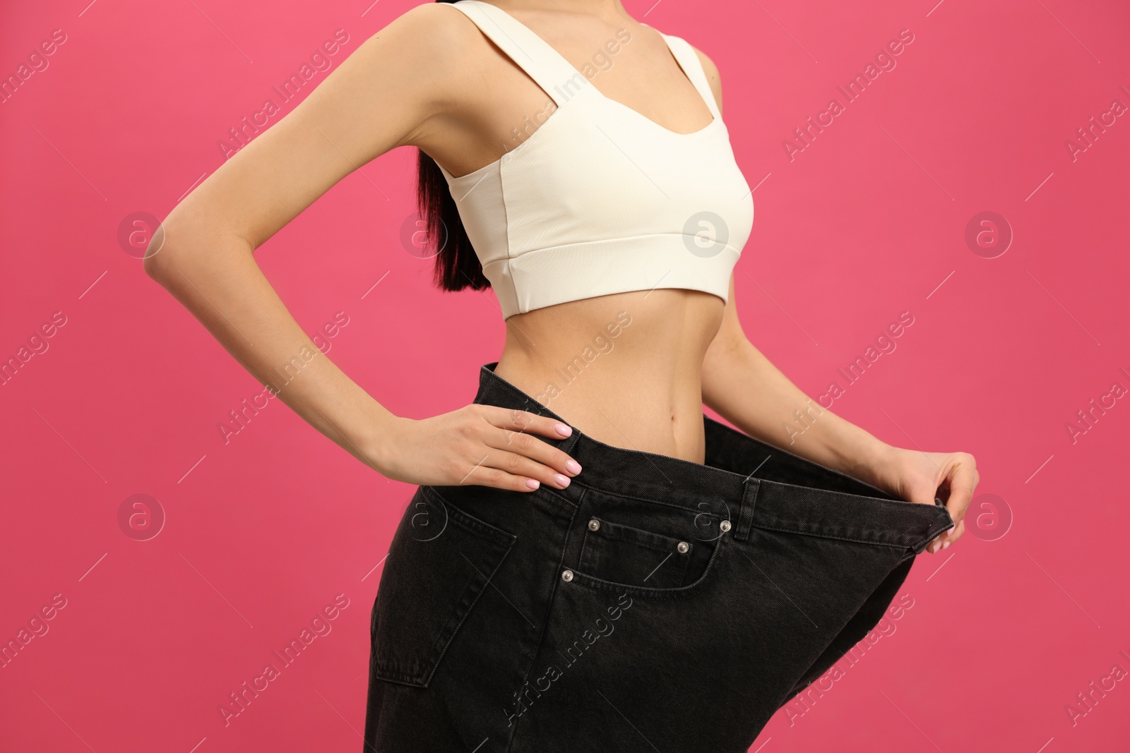 Photo of Young woman wearing big jeans after weight loss on pink background, closeup