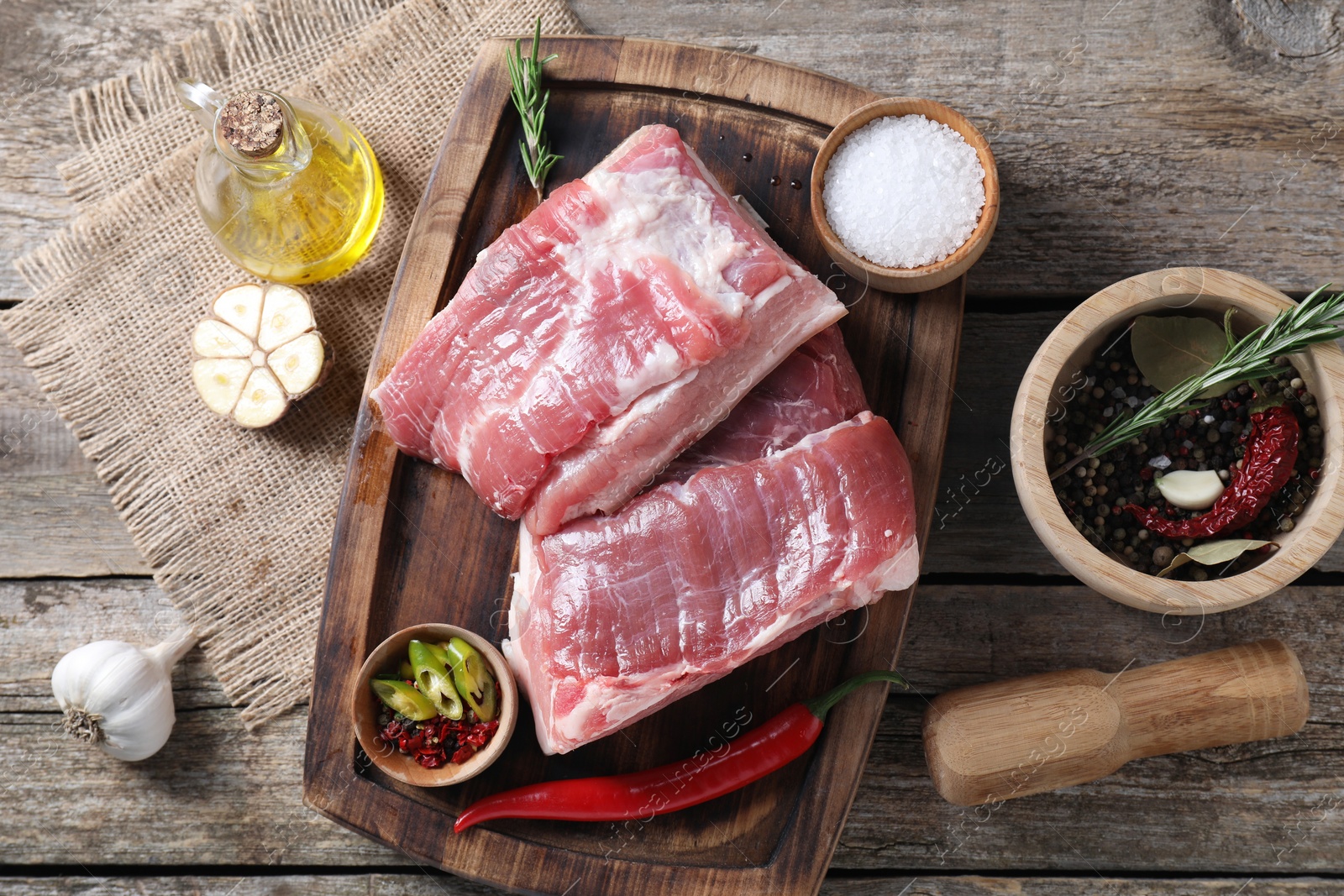 Photo of Pieces of raw pork belly, oil, garlic, salt and spices on wooden table, flat lay