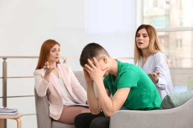 Young female psychologist working with teenage boy and his mother in office