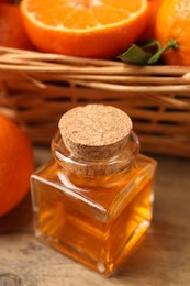 Photo of Bottle of tangerine essential oil and fresh fruits on wooden table, closeup