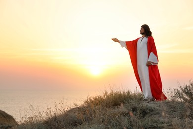 Photo of Jesus Christ raising hand on hills at sunset. Space for text