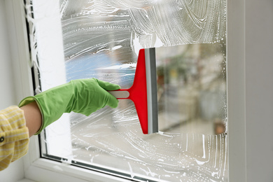 Photo of Woman cleaning window with squeegee indoors, closeup