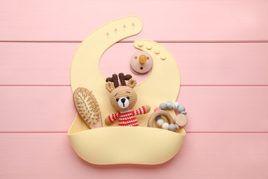 Photo of Flat lay composition with silicone baby bib, toys and accessories on pink wooden background