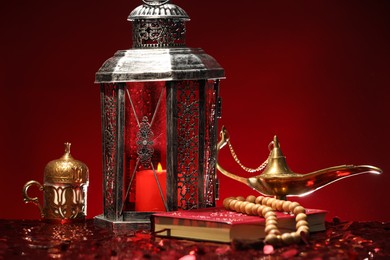 Arabic lantern, Quran, misbaha and Aladdin magic lamp on shiny red table