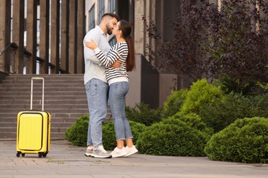 Photo of Long-distance relationship. Beautiful young couple kissing and suitcase near building outdoors