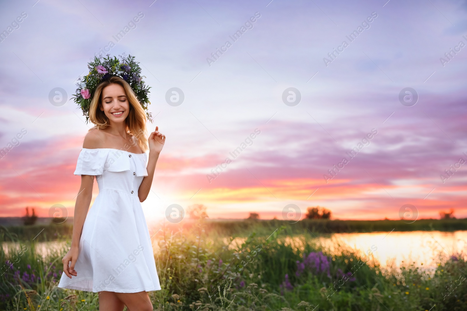 Photo of Young woman wearing wreath made of beautiful flowers outdoors at sunset