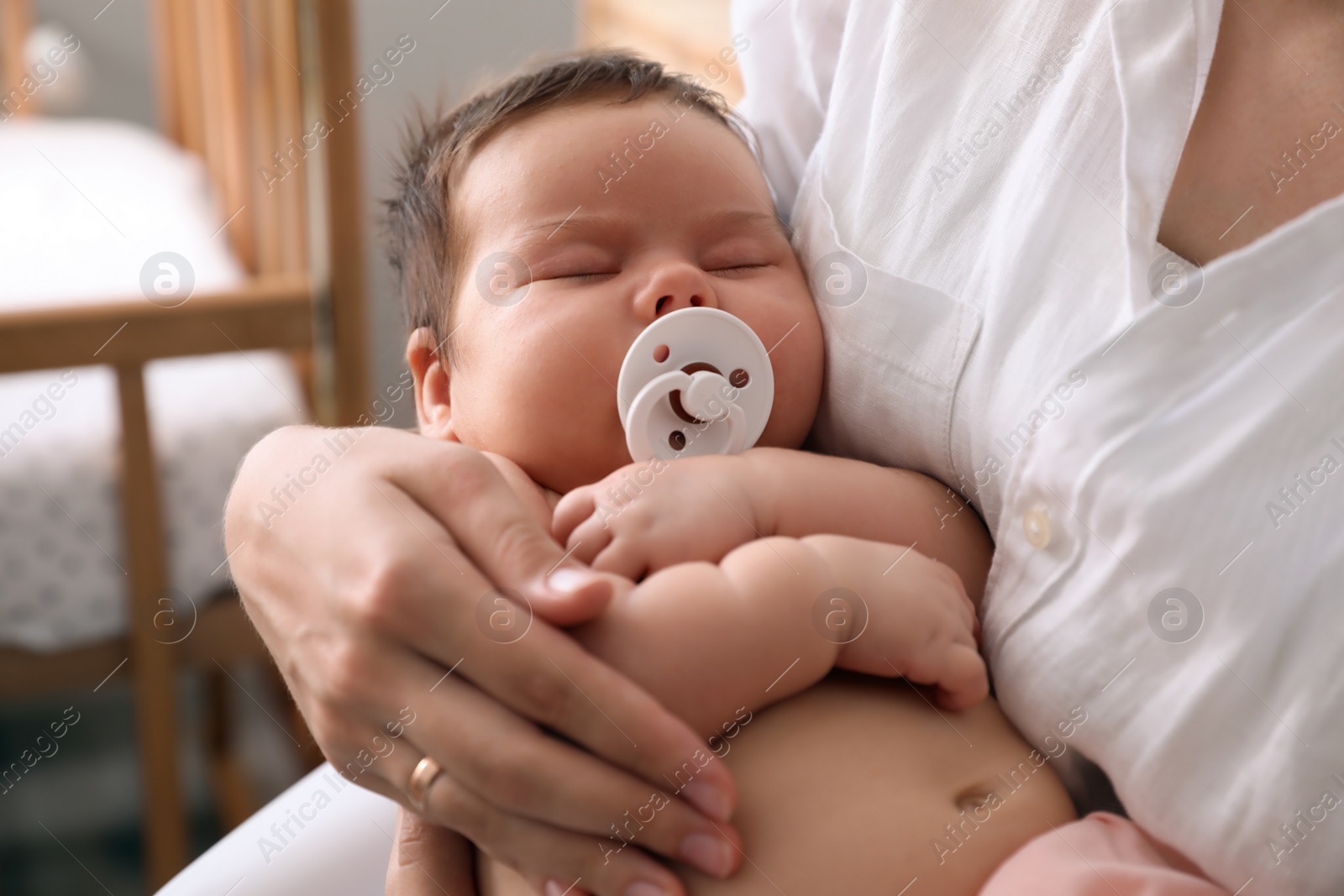 Photo of Mother holding her cute little baby with pacifier at home, closeup