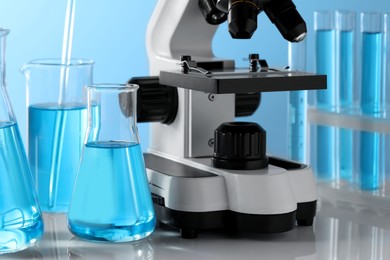 Different laboratory glassware, test tubes with light blue liquid and microscope on table