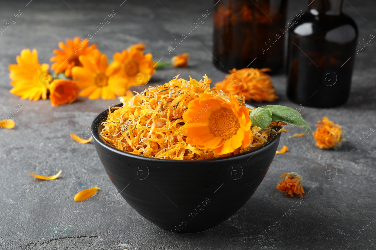 Photo of Bowl of dry and fresh calendula flowers on grey table