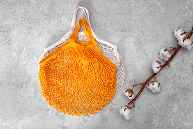 Net bags and cotton branch on light grey table, top view