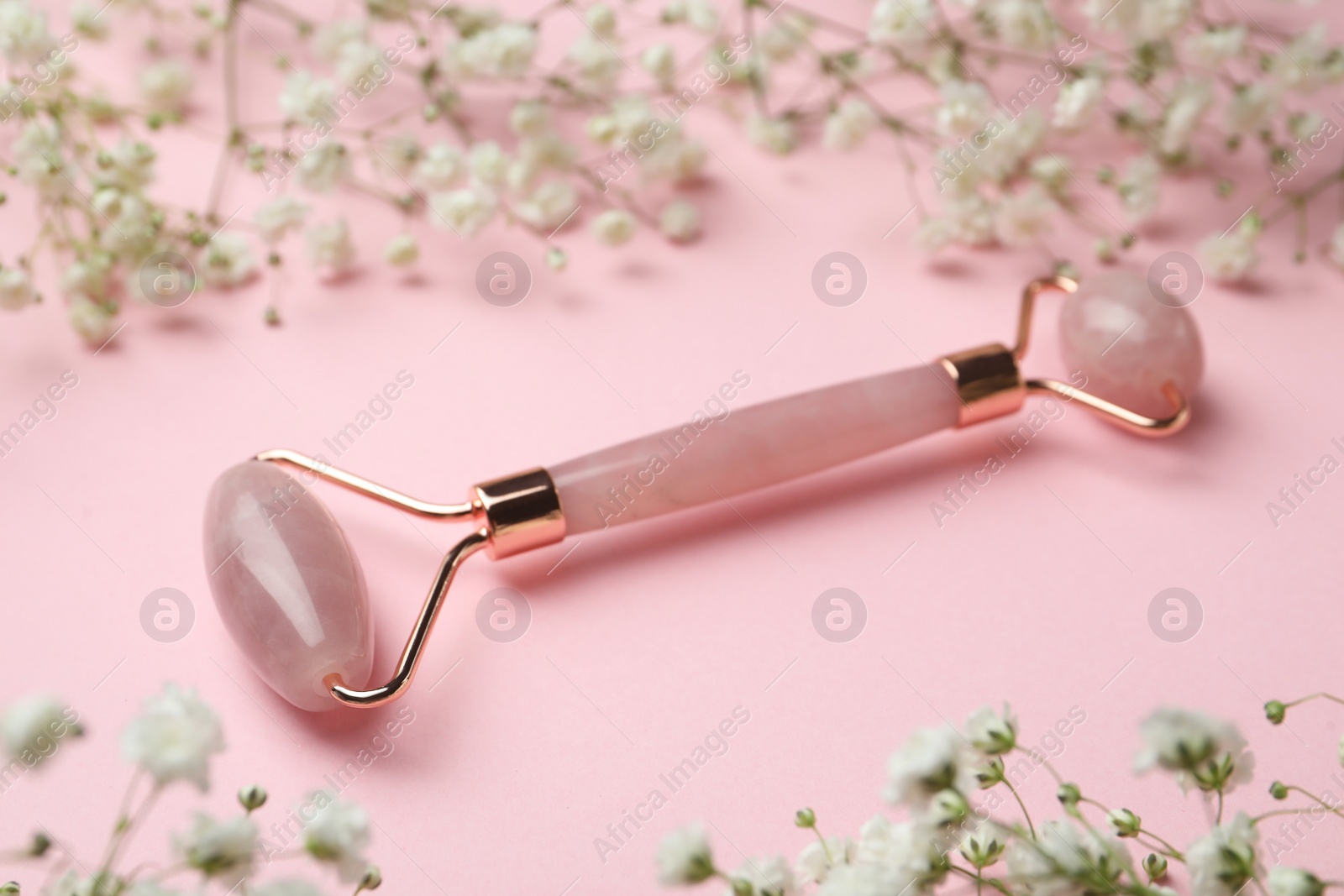 Photo of Natural face roller and flowers on pink background