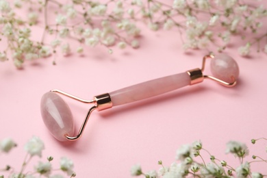 Natural face roller and flowers on pink background