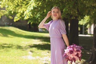 Beautiful woman with bouquet of spring flowers in park on sunny day, space for text