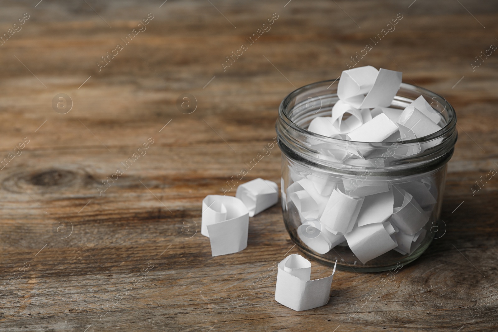 Photo of Glass jar with paper pieces on wooden table, space for text