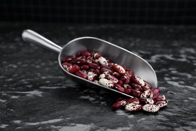Photo of Metal scoop with dry kidney beans on black textured table