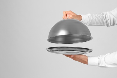 Photo of Waiter holding metal tray with lid on light background