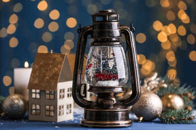 Photo of Beautiful snow globe in vintage lantern and Christmas decor on table against festive lights