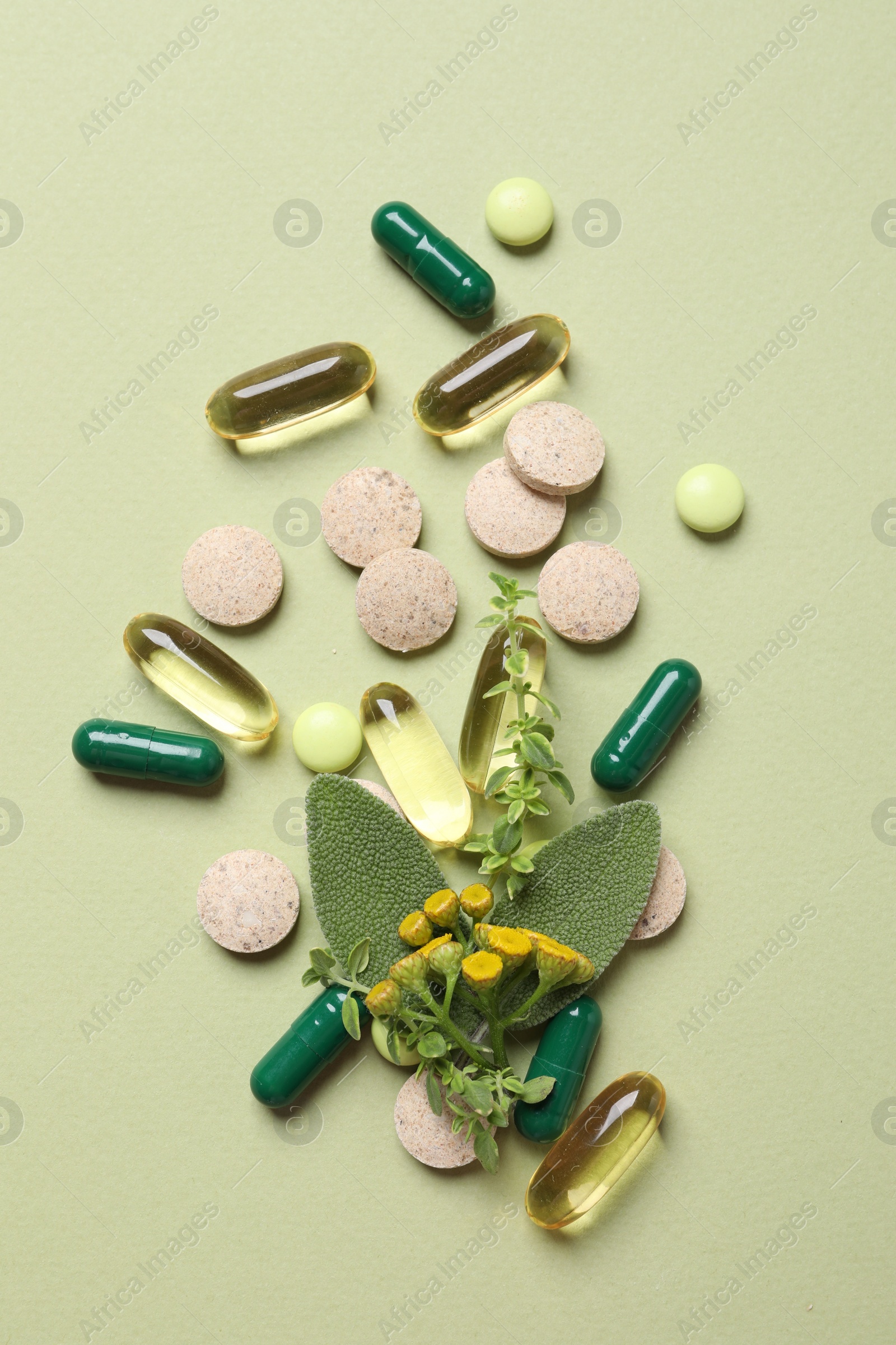 Photo of Different pills and herbs on light green background, flat lay. Dietary supplements