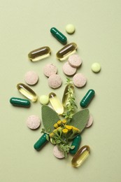 Photo of Different pills and herbs on light green background, flat lay. Dietary supplements