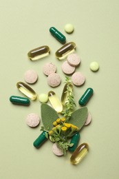 Different pills and herbs on light green background, flat lay. Dietary supplements