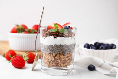 Photo of Tasty granola with berries, yogurt and chia seeds in glass on white table