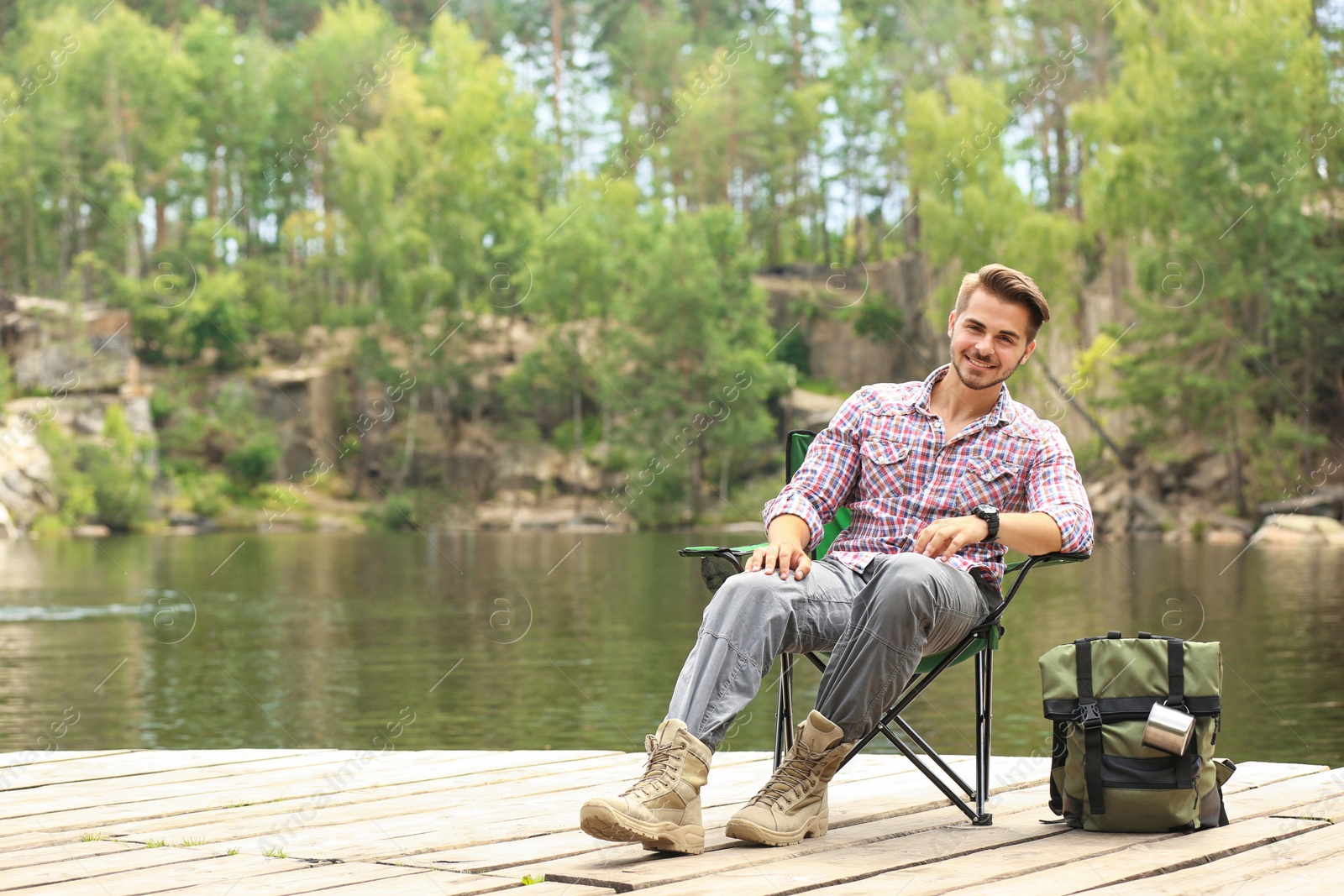 Photo of Young man resting on wooden pier near lake. Camping season