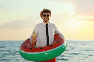 Photo of Happy man with inflatable ring and beer on beach. Business trip