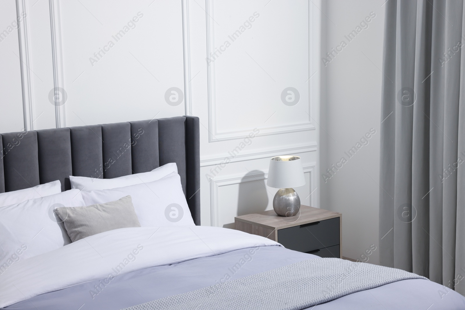 Photo of Comfortable bed near bedside table with lamp in stylish bedroom