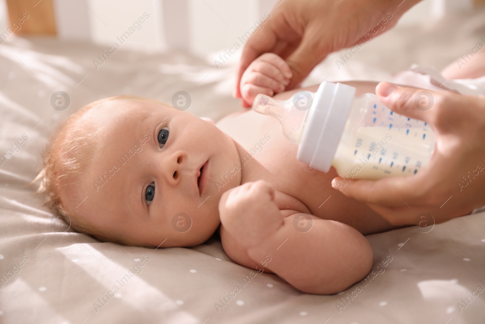 Photo of Mother feeding cute little baby with milk in cot, closeup. Healthy lifestyle
