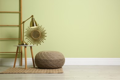 Stylish room interior with comfortable knitted pouf and decor elements near light green wall, space for text