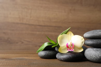 Spa stones, beautiful orchid flower and bamboo sprout on wooden table. Space for text