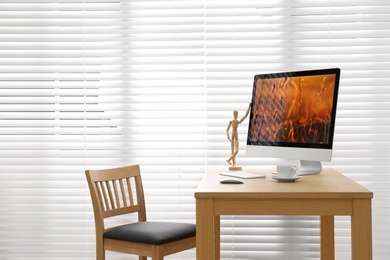 Modern PC on table near window with blinds in room