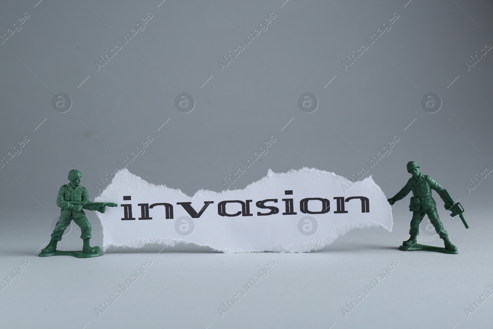 Photo of Paper with word Invasion and toy soldiers on light grey background