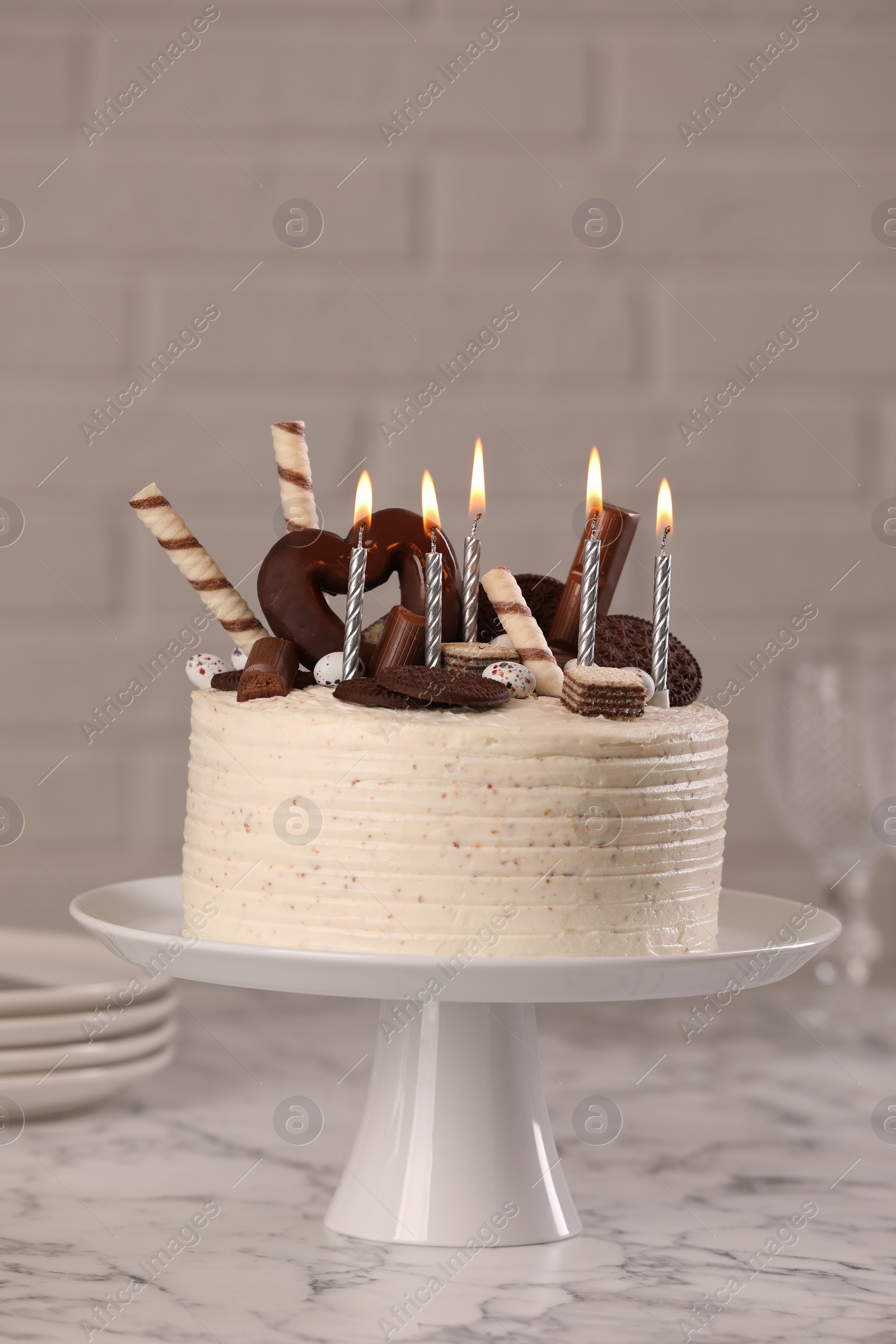 Photo of Delicious cake decorated with sweets and burning candles on white marble table